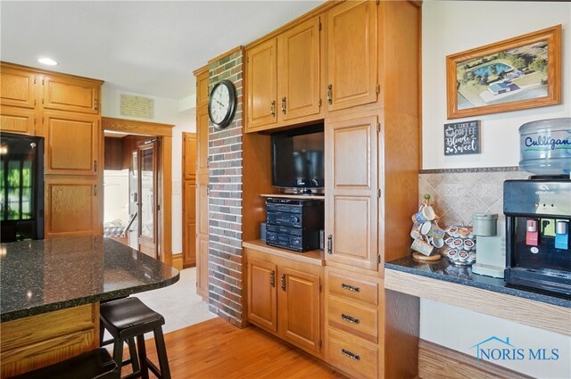 1482 Township Road 55, Ada, OH 45810 - kitchen with tasteful backsplash, dark stone counters, a kitchen bar, black fridge, and light wood-type flooring