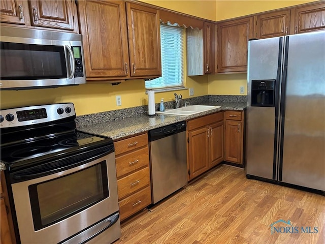 6955 Dorr St Unit 56, Toledo, OH 43615 - kitchen with appliances with stainless steel finishes, a sink, brown cabinetry, light wood-type flooring, and dark stone countertops