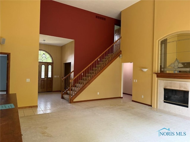 8411 Willow Glen Ct, Holland, OH 43528 - unfurnished living room with a towering ceiling, stairway, carpet flooring, tile patterned flooring, and a tile fireplace