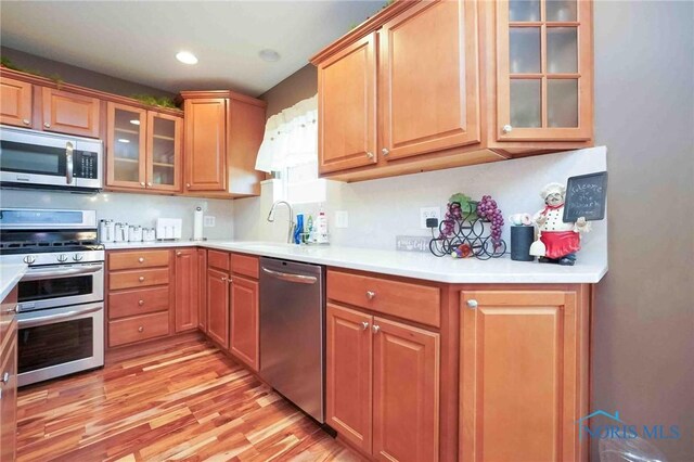 501 Flintlock Ct, Findlay, OH 45840 - kitchen featuring stainless steel appliances, a sink, light wood-type flooring, light countertops, and glass insert cabinets