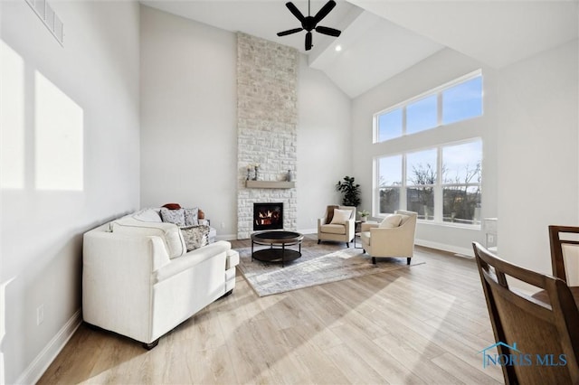 living room with high vaulted ceiling, a ceiling fan, wood finished floors, a stone fireplace, and baseboards