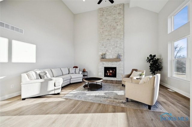 living area featuring high vaulted ceiling, ceiling fan, wood finished floors, a stone fireplace, and baseboards