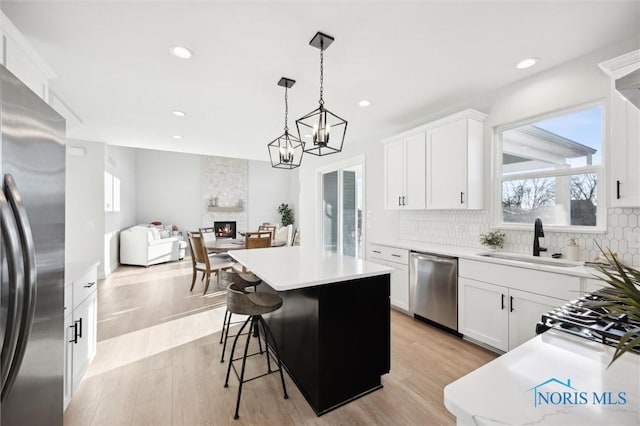 kitchen with stainless steel appliances, a sink, a kitchen island, decorative backsplash, and a fireplace