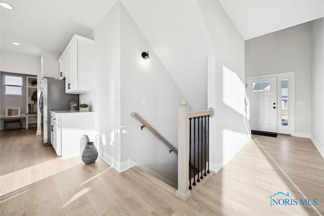 foyer featuring light wood-type flooring, baseboards, a towering ceiling, and recessed lighting