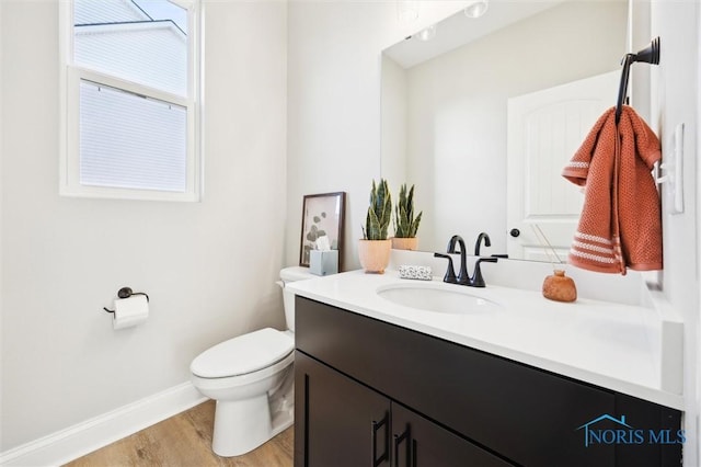 half bath with toilet, baseboards, wood finished floors, and vanity