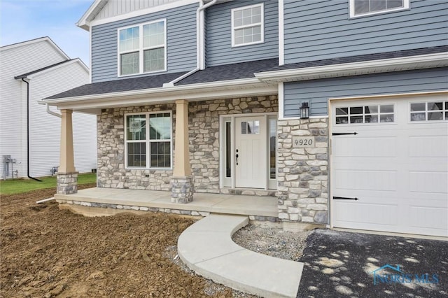 entrance to property featuring covered porch, stone siding, and roof with shingles