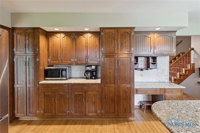 2142 Tracy Rd, Northwood, OH 43619 - kitchen with stainless steel microwave, light wood-style floors, brown cabinetry, tasteful backsplash, and light stone countertops