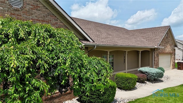 12327 Buckeye Dr, Paulding, OH 45879 - view of property exterior with roof with shingles, brick siding, an attached garage, a porch, and concrete driveway