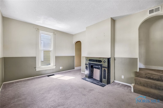 446 Center St, Findlay, OH 45840 - unfurnished living room with arched walkways, a textured ceiling, wainscoting, carpet, and stairs