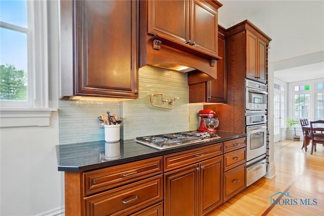 1100 S Main St, Findlay, OH 45840 - kitchen with stainless steel appliances, a warming drawer, decorative backsplash, light wood-style floors, and dark stone countertops