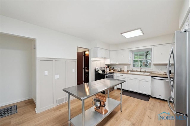 2222 Talmadge Rd, Ottawa Hills, OH 43606 - kitchen with stainless steel appliances, a sink, white cabinetry, light wood-type flooring, and a wainscoted wall