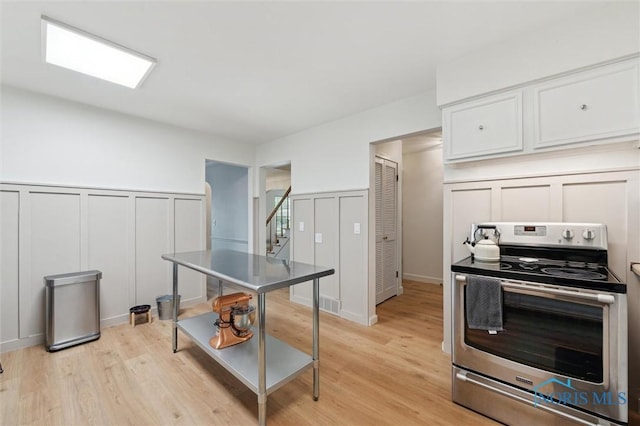 2222 Talmadge Rd, Ottawa Hills, OH 43606 - kitchen with stainless steel electric stove, a decorative wall, white cabinets, light wood-type flooring, and a wainscoted wall
