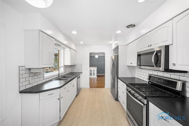 4550 W Sylvania Ave, Toledo, OH 43623 - kitchen featuring appliances with stainless steel finishes, a sink, dark countertops, white cabinetry, and light wood finished floors