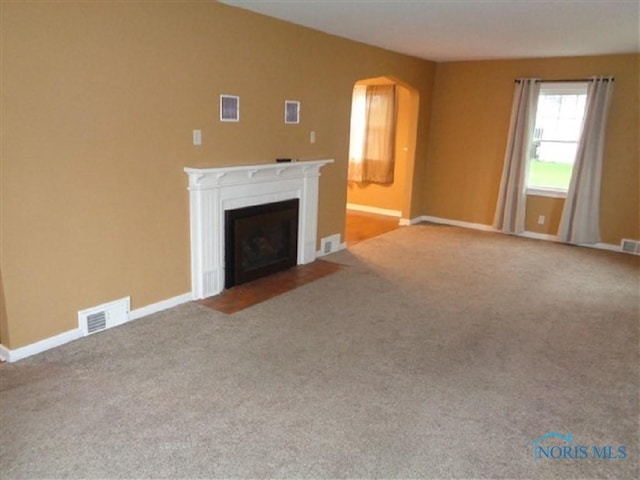 934 E 4th St, Ottawa, OH 45875 - unfurnished living room with a fireplace with flush hearth, carpet, arched walkways, and baseboards