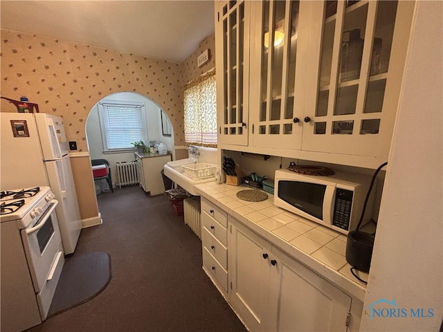 181 Osborne St, Rossford, OH 43460 - kitchen with tile counters, white appliances, wallpapered walls, radiator, and white cabinets
