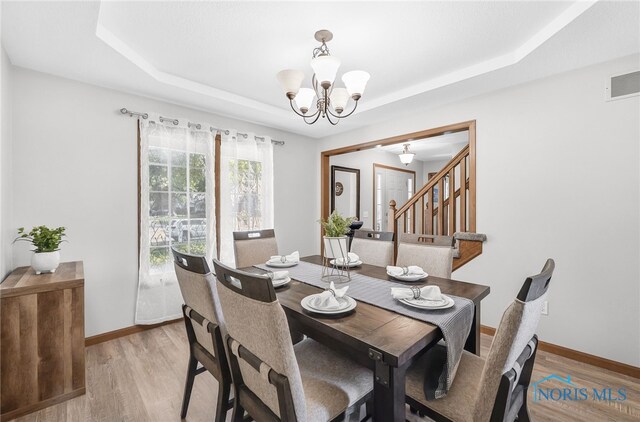 8225 Hidden Forest Dr, Holland, OH 43528 - dining room with a tray ceiling, light wood-style floors, a chandelier, and baseboards