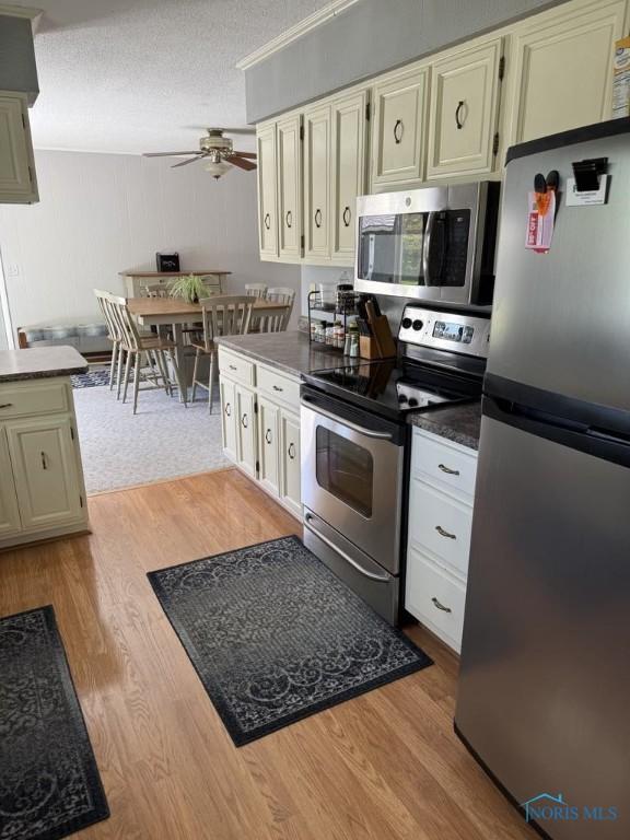 1133 Inverness Dr, Findlay, OH 45840 - kitchen with stainless steel appliances, a ceiling fan, wood finished floors, dark countertops, and a textured ceiling