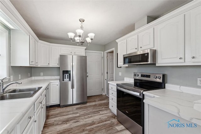 1250 Indiana Ave, Napoleon, OH 43545 - kitchen featuring stainless steel appliances, a sink, a chandelier, white cabinets, and light wood-style floors
