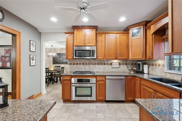 2256 Barrington Dr, Toledo, OH 43606 - kitchen with appliances with stainless steel finishes, dark stone counters, decorative backsplash, brown cabinetry, and recessed lighting