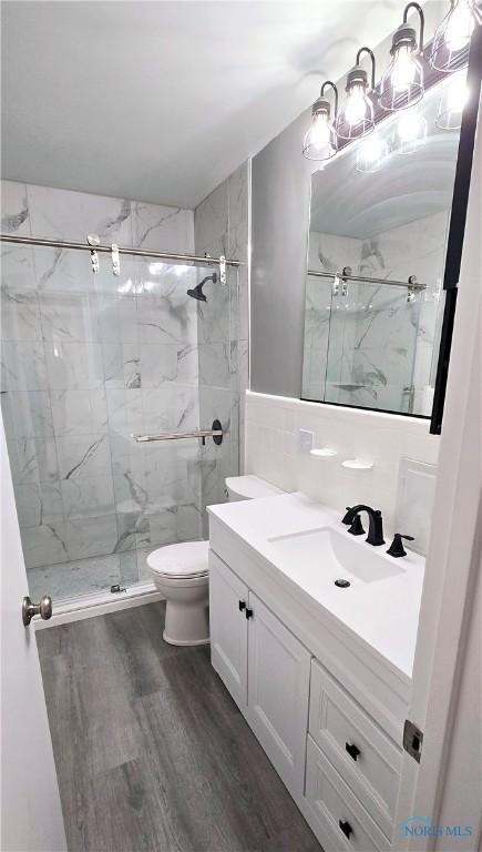 2621 Gloria Ct, Toledo, OH 43614 - bathroom featuring wood finished floors, vanity, toilet, a marble finish shower, and tile walls