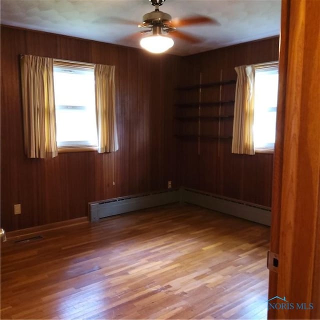 15979 Hill Rd, Defiance, OH 43512 - empty room featuring a ceiling fan, light wood-style flooring, wood walls, and a baseboard radiator