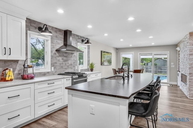 2714 W Rockridge Cir, Toledo, OH 43606 - kitchen with wall chimney exhaust hood, a sink, high end stainless steel range oven, a breakfast bar, and an island with sink