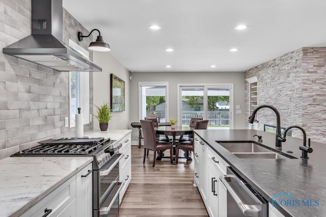 2714 W Rockridge Cir, Toledo, OH 43606 - kitchen with wall chimney exhaust hood, appliances with stainless steel finishes, a sink, dark stone countertops, and wood finished floors