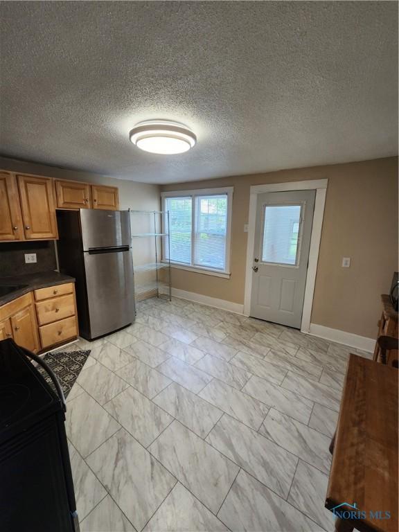 815 S Blanchard St, Findlay, OH 45840 - kitchen featuring freestanding refrigerator, baseboards, dark countertops, light marble finish flooring, and a textured ceiling