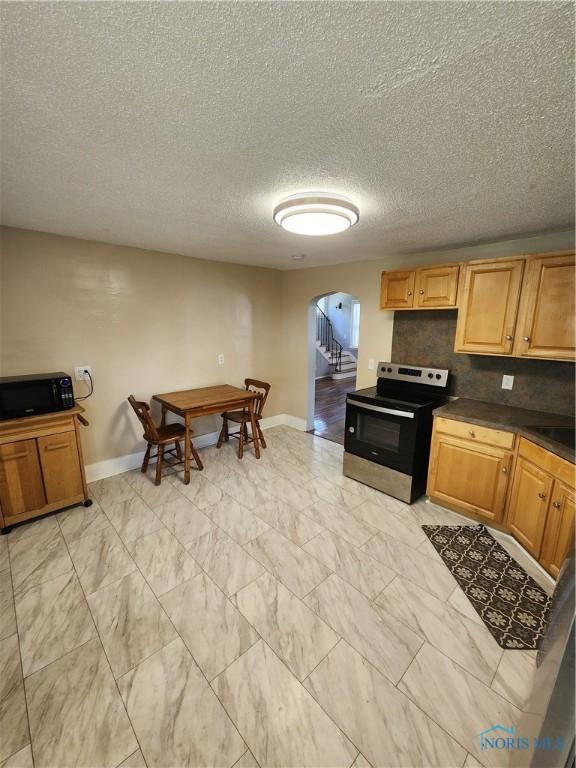 815 S Blanchard St, Findlay, OH 45840 - kitchen featuring stainless steel range with electric stovetop, arched walkways, black microwave, baseboards, and a textured ceiling