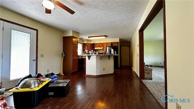 13926 Rd 154, Paulding, OH 45879 - kitchen with a breakfast bar, under cabinet range hood, dark wood-style floors, a textured ceiling, and a ceiling fan