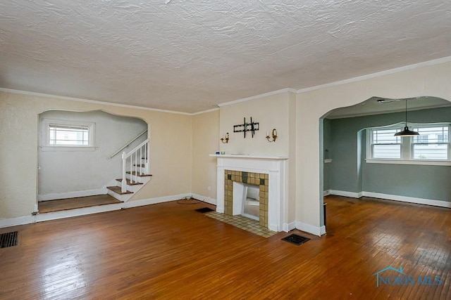 3819 Rushland Ave, Toledo, OH 43613 - unfurnished living room with hardwood / wood-style floors, a tiled fireplace, ornamental molding, arched walkways, and a textured ceiling