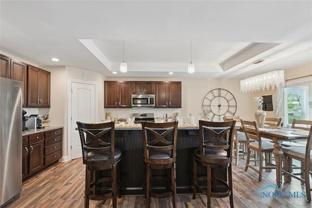 10 Hidden Village Ln, Holland, OH 43528 - kitchen featuring appliances with stainless steel finishes, a raised ceiling, dark wood finished floors, decorative backsplash, and a kitchen breakfast bar