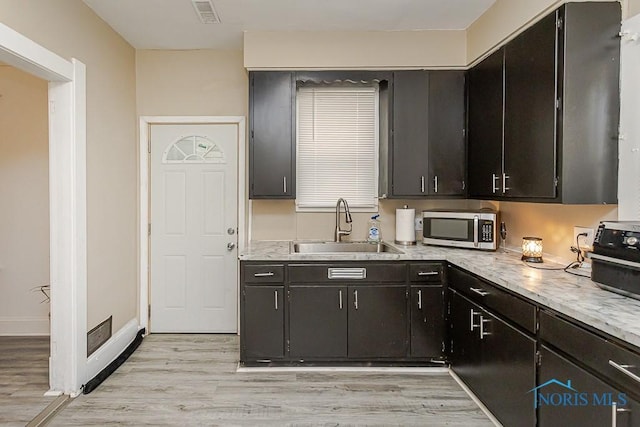 1129 Mason St, Toledo, OH 43605 - kitchen featuring stainless steel microwave, a sink, light wood-type flooring, light countertops, and baseboards