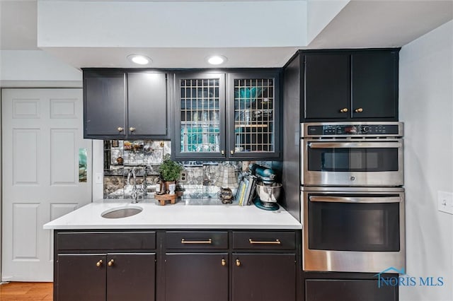 4723 High Oaks Blvd, Toledo, OH 43623 - kitchen featuring stainless steel double oven, a sink, light countertops, glass insert cabinets, and backsplash