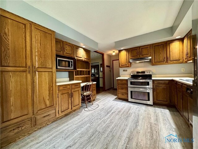 1508 Darbyshire Dr, Defiance, OH 43512 - kitchen with stainless steel appliances, under cabinet range hood, light wood finished floors, brown cabinetry, and light countertops