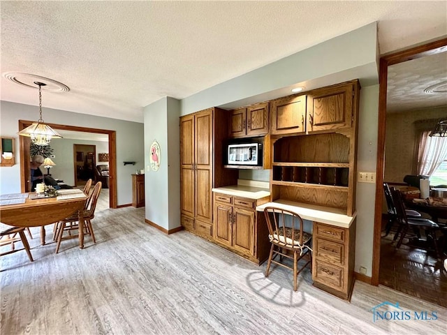 1508 Darbyshire Dr, Defiance, OH 43512 - kitchen with a textured ceiling, brown cabinets, a desk, light wood-style flooring, and pendant lighting