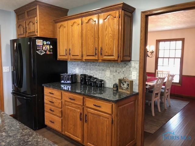 415 W Jamestown Ave, Tiffin, OH 44883 - kitchen with freestanding refrigerator, dark wood-style floors, brown cabinets, tasteful backsplash, and dark stone countertops