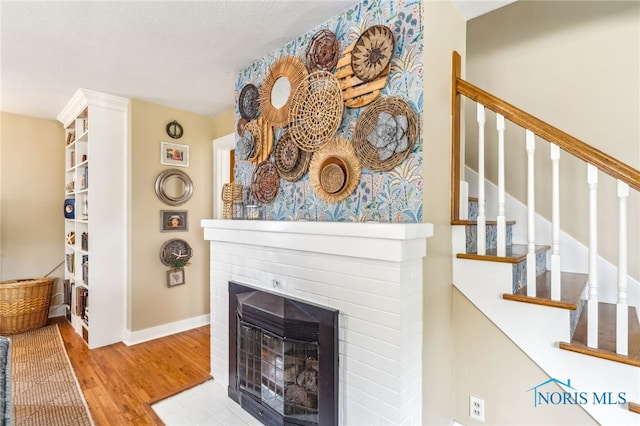 713 N Vine St, Fostoria, OH 44830 - living area featuring a brick fireplace, wood finished floors, stairway, and baseboards