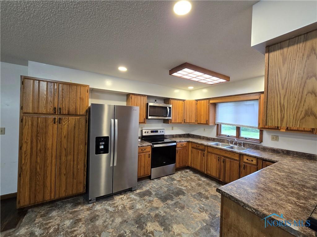 711 Circle Dr, Fostoria, OH 44830 - kitchen with appliances with stainless steel finishes, dark countertops, brown cabinetry, a sink, and recessed lighting