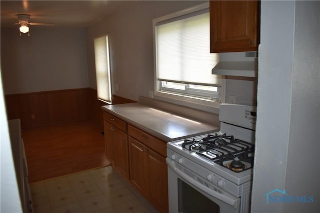 38 N Melody Ln, Waterville, OH 43566 - kitchen featuring white gas stove, exhaust hood, a ceiling fan, a wainscoted wall, and light flooring