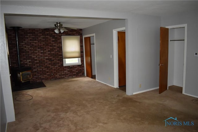 38 N Melody Ln, Waterville, OH 43566 - unfurnished living room with a wood stove, a ceiling fan, brick wall, carpet floors, and baseboards