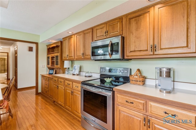 1008 Muirfield Dr, Findlay, OH 45840 - kitchen featuring appliances with stainless steel finishes, light countertops, light wood-style floors, brown cabinetry, and baseboards