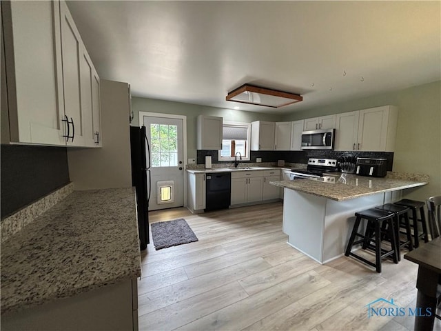 803 W Holland St, Archbold, OH 43502 - kitchen with black appliances, a peninsula, light wood finished floors, and light stone countertops