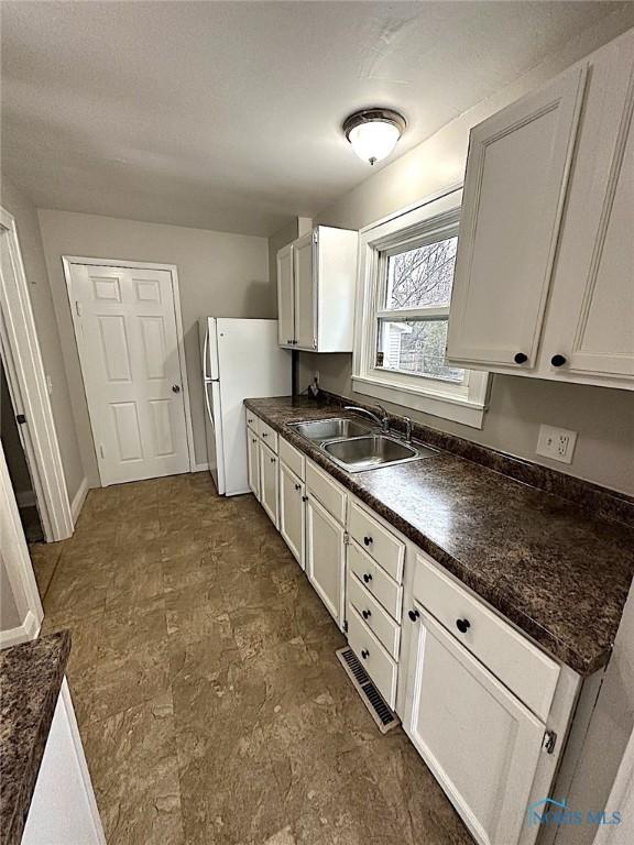 1739 Wyndhurst Rd, Toledo, OH 43607 - kitchen with a sink, dark countertops, freestanding refrigerator, white cabinets, and baseboards