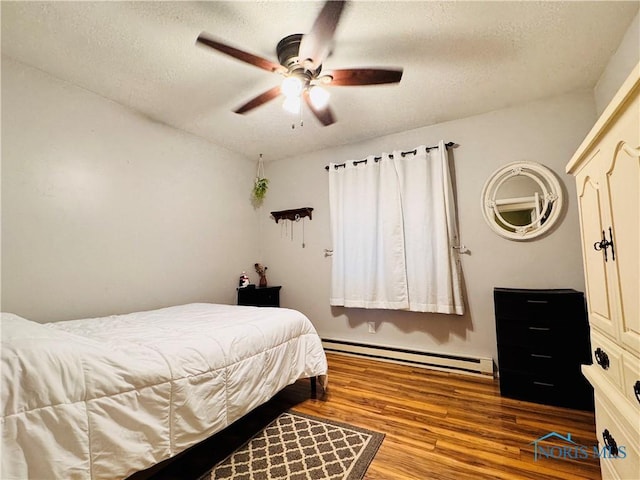 1019 E Wilson St, Bryan, OH 43506 - bedroom featuring baseboard heating, wood finished floors, a textured ceiling, a ceiling fan, and baseboards