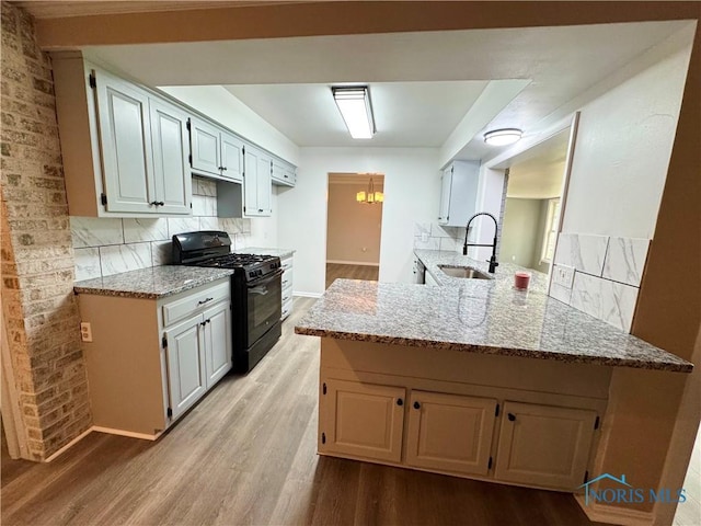 2102 Glen Arbor Dr, Toledo, OH 43614 - kitchen featuring black range with gas stovetop, a sink, light wood-type flooring, light stone counters, and a peninsula