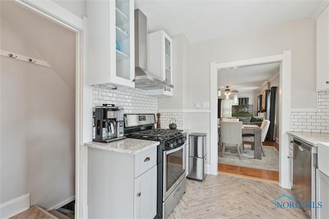 2707 Gunckel Blvd, Toledo, OH 43606 - kitchen with stainless steel appliances, wall chimney range hood, backsplash, a ceiling fan, and white cabinetry
