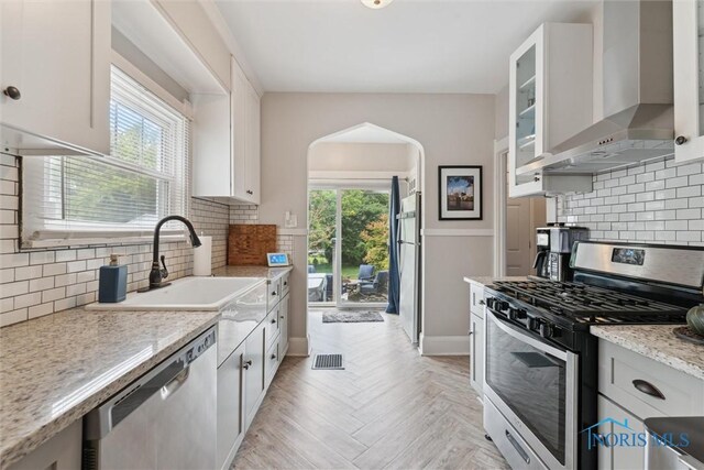 2707 Gunckel Blvd, Toledo, OH 43606 - kitchen featuring appliances with stainless steel finishes, wall chimney range hood, arched walkways, and decorative backsplash