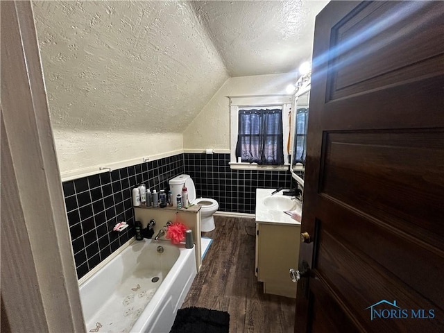 609 E Broadway St, Toledo, OH 43605 - bathroom featuring a textured ceiling, vanity, vaulted ceiling, a garden tub, and wood finished floors
