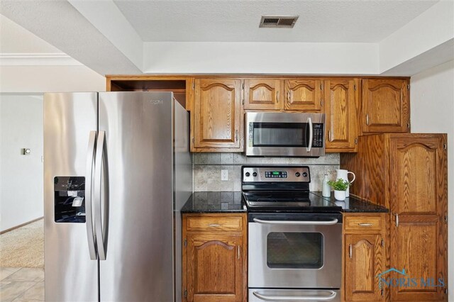 17715 Mitchell Rd, Bowling Green, OH 43402 - kitchen with stainless steel appliances, brown cabinets, tasteful backsplash, and dark stone countertops